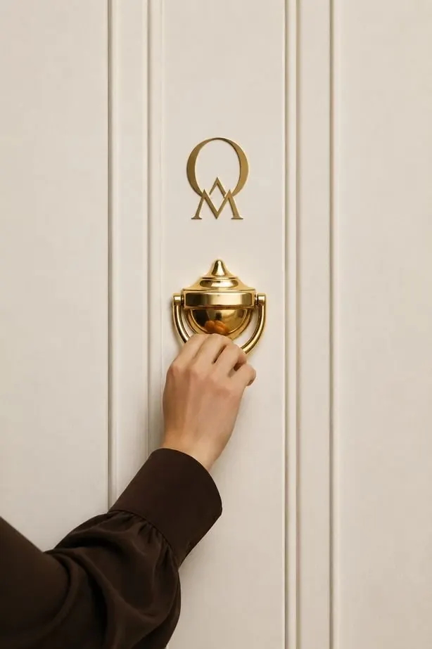 A hand on a brass door knocker beneath the ORMONT monogram